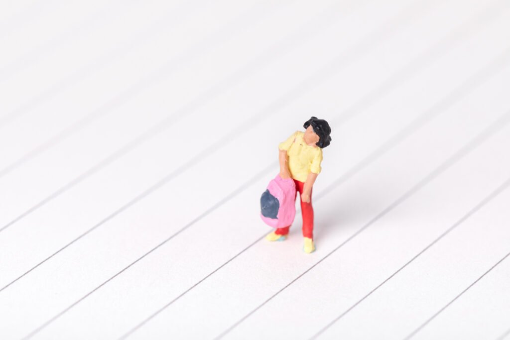 A small, miniature figure stands with its head bowed down, holding a pink bag. This image represents the feeling of low self-esteem and dejection.