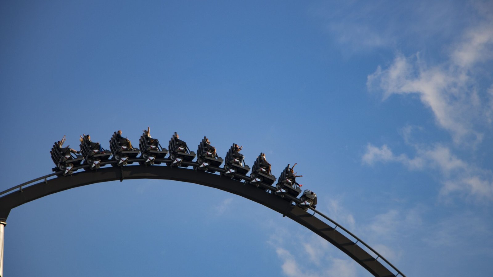 A black rollercoaster car travels along a curved track against a blue sky with a few clouds. This image represents the cyclical highs and lows experienced by individuals with bipolar disorder.