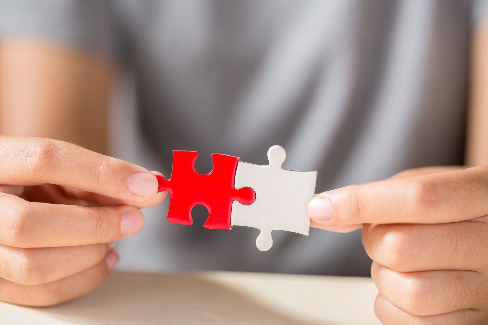 Two hands connecting red and white puzzle pieces, symbolizing the importance of communication and collaboration in addressing relationship challenges and sexual concerns.